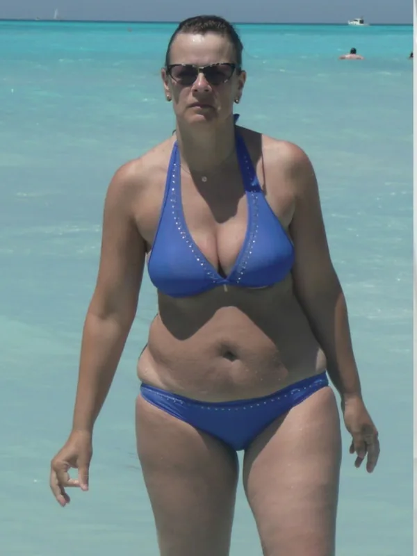 Femme en maillot de bain bleu debout dans l'eau claire d'une plage tropicale sous un ciel bleu.