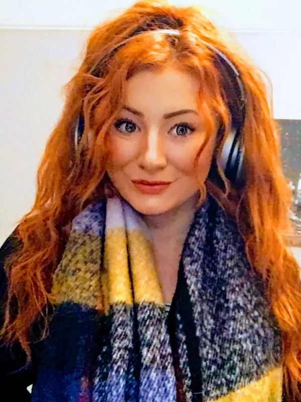 Portrait d'une femme aux cheveux roux portant des écouteurs et un écharpe colorée, regardant l'objectif.