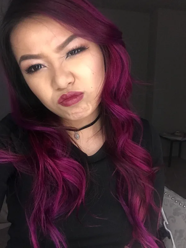 Portrait d'une femme aux cheveux violets portant un haut noir et un collier choker, faisant une grimace vers l'objectif.