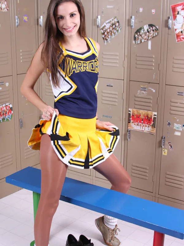 Jeune femme en tenue de cheerleader posant sur une banquette devant des casiers scolaires.